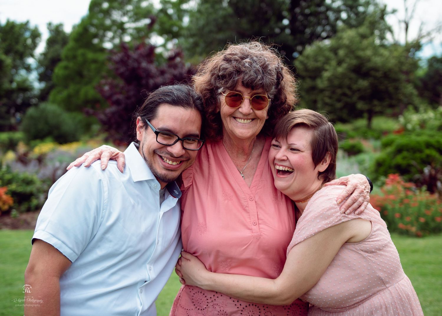 Three friends share joyful laughter while embracing in a garden setting.