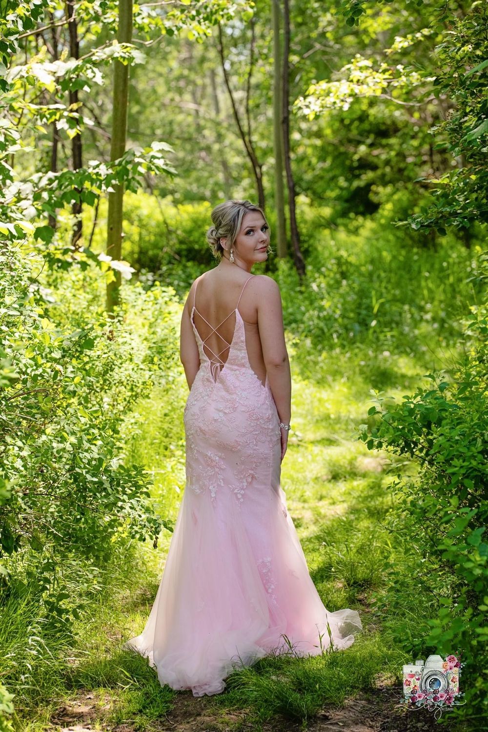 Back view of blush pink lace wedding gown with delicate detail in woodland setting.