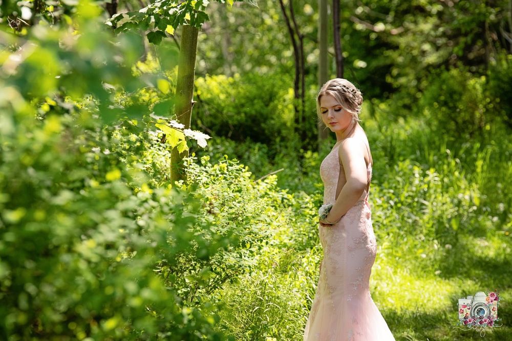 Soft pink bridal gown captured in dappled sunlight among green forest foliage.