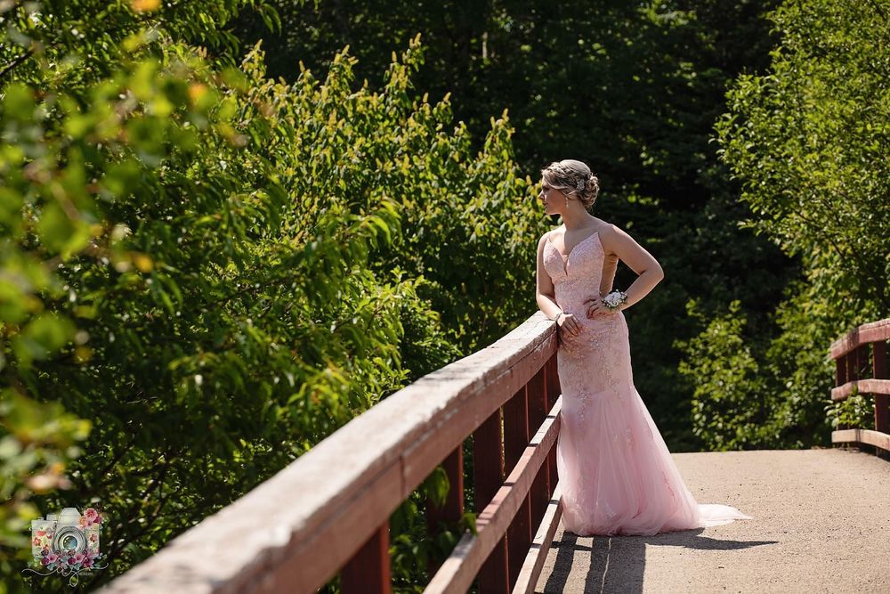 Blush wedding dress silhouette posed on wooden bridge in forest setting.
