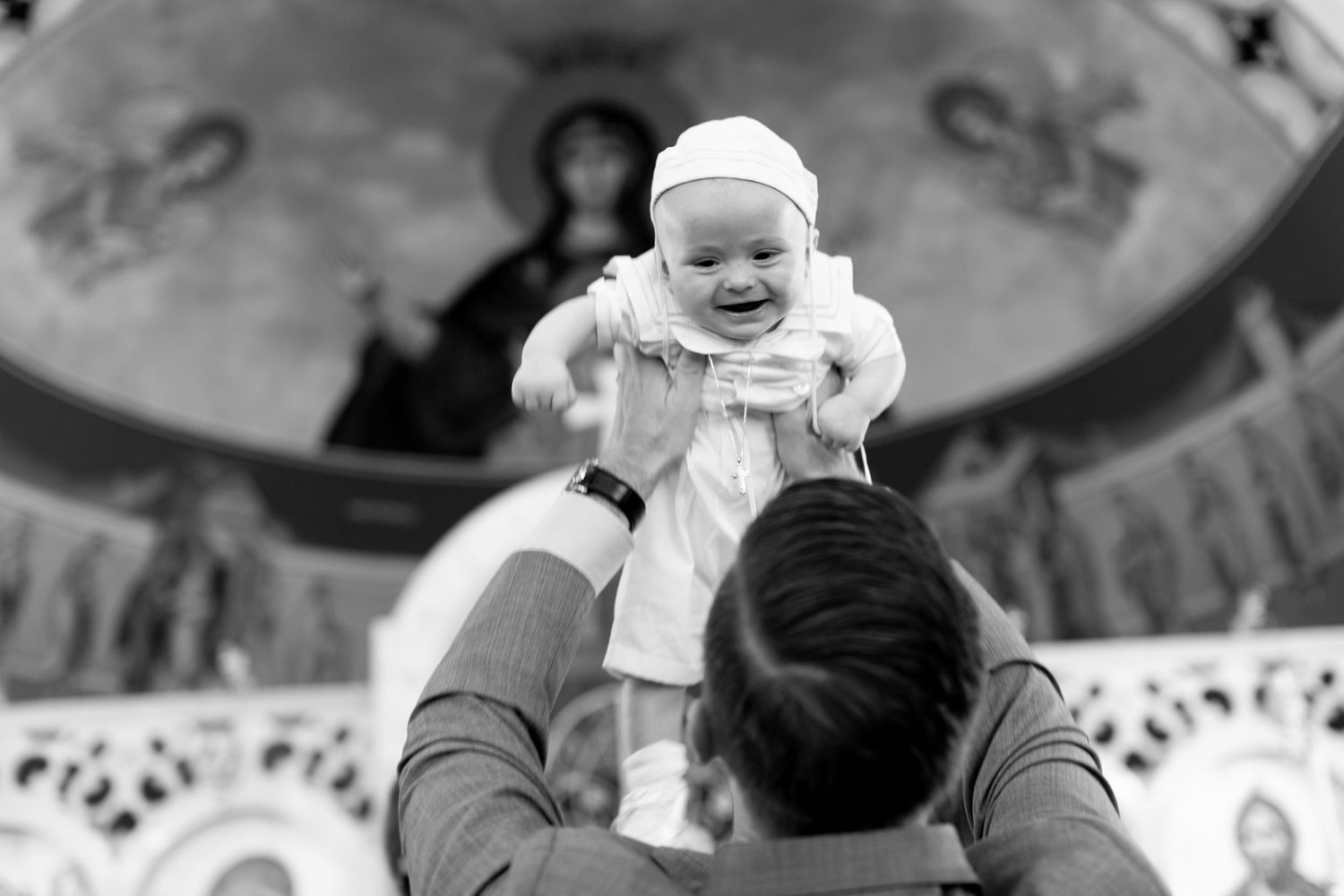 Black and white photo of baby being lifted up high inside ornate building.