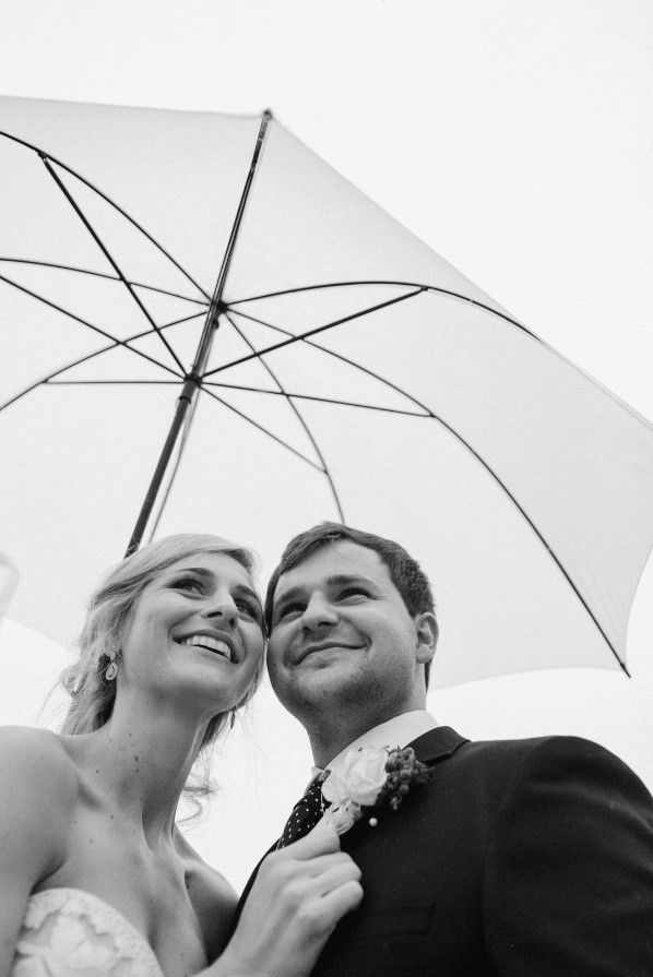 Hiding under a umbrella at Florence wedding venue, a wedding couple is shielded from the pouring rain.