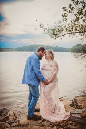 A couple shares an intimate moment by the water's edge in formal attire.
