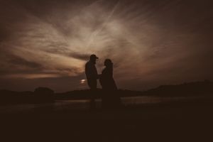Two silhouettes share an intimate moment against a dramatic sunset sky.