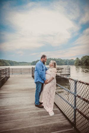 A romantic couple poses on a wooden dock overlooking a peaceful lake.