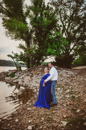 A romantic moment captured on a rocky shoreline with trees in the background.