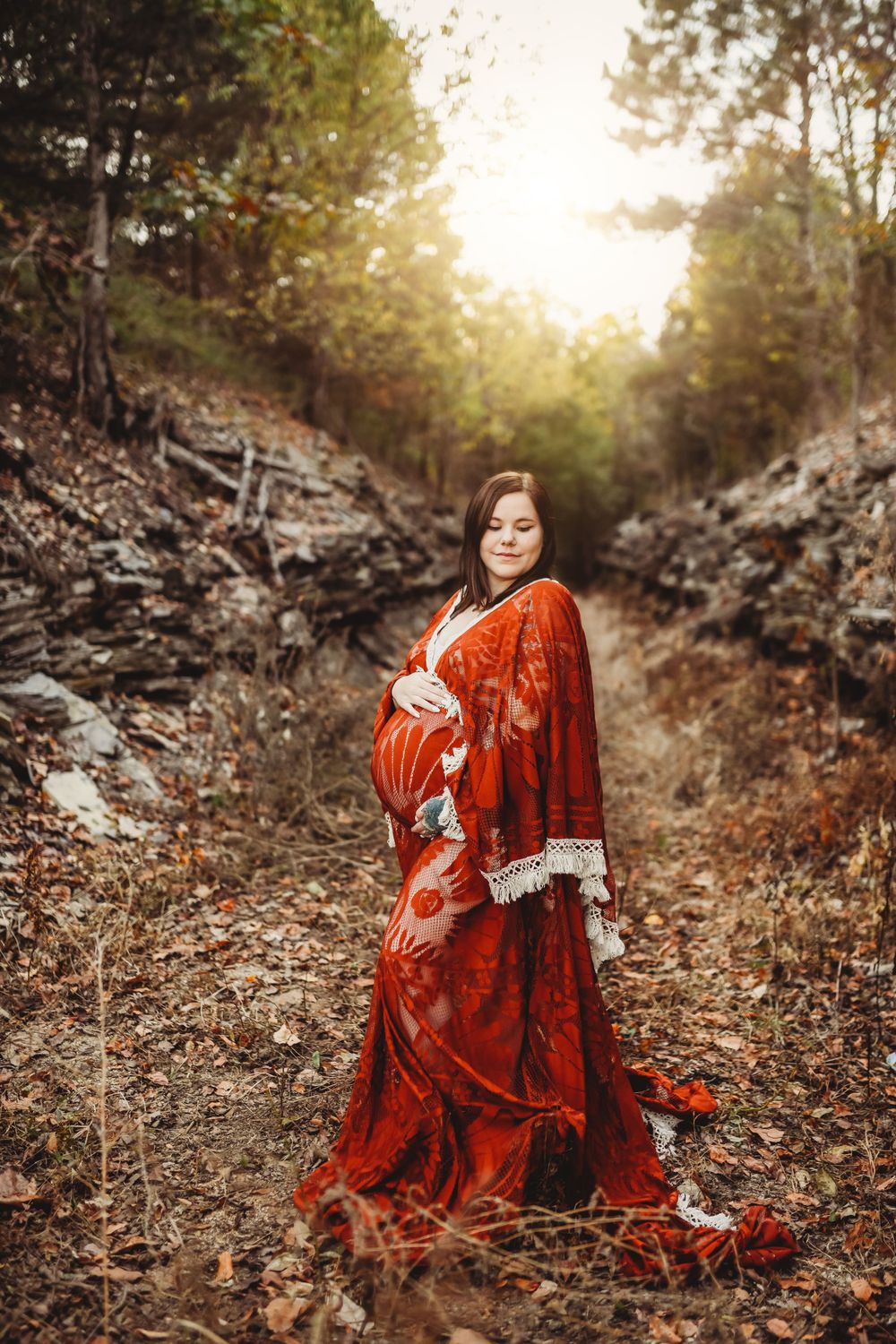 Autumn maternity photoshoot featuring a flowing red velvet dress in a rustic outdoor setting.