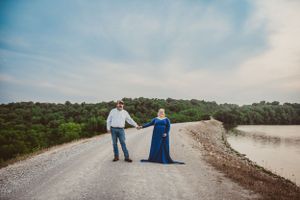 A couple holding hands on a gravel road beside a scenic lake.