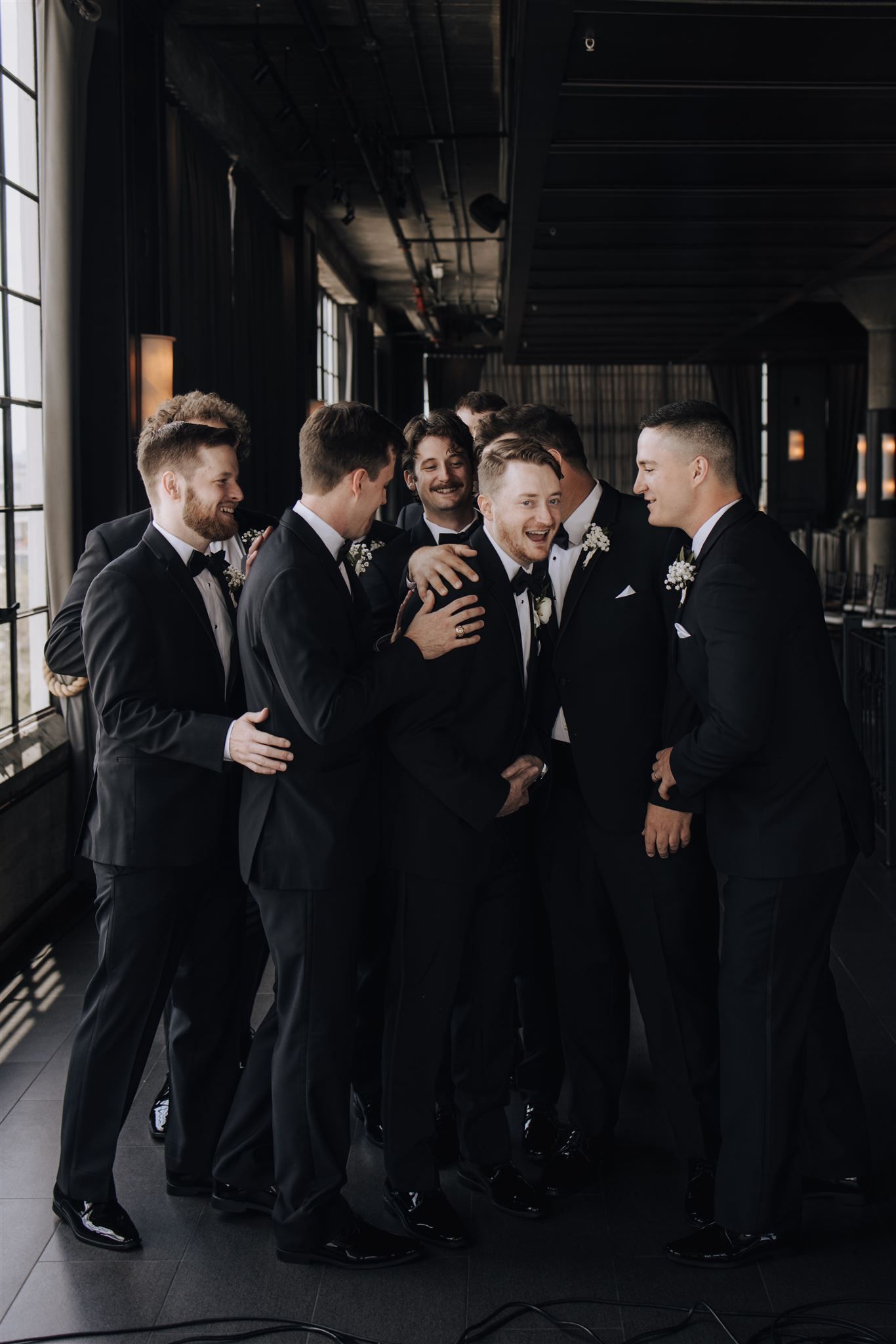 A group laughs together in formal attire during a wedding celebration.