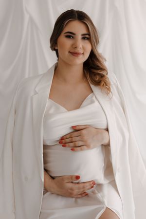 A classic maternity portrait showing a woman in white with soft makeup and styled waves.