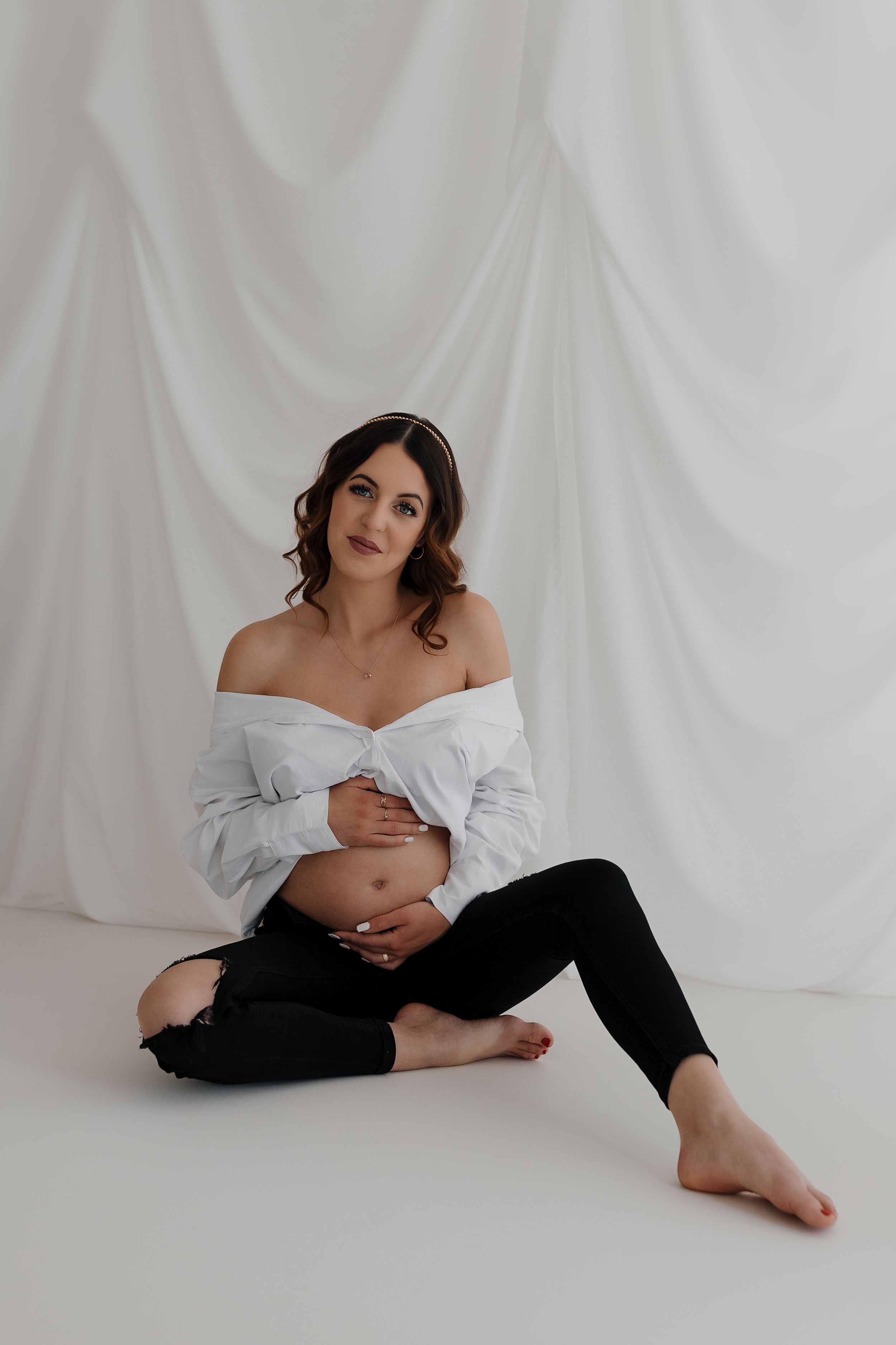 Artistic maternity photo of expecting mother in white top and black pants on white background.