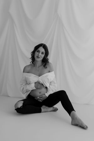 Black and white maternity portrait with dramatic lighting and minimalist styling.