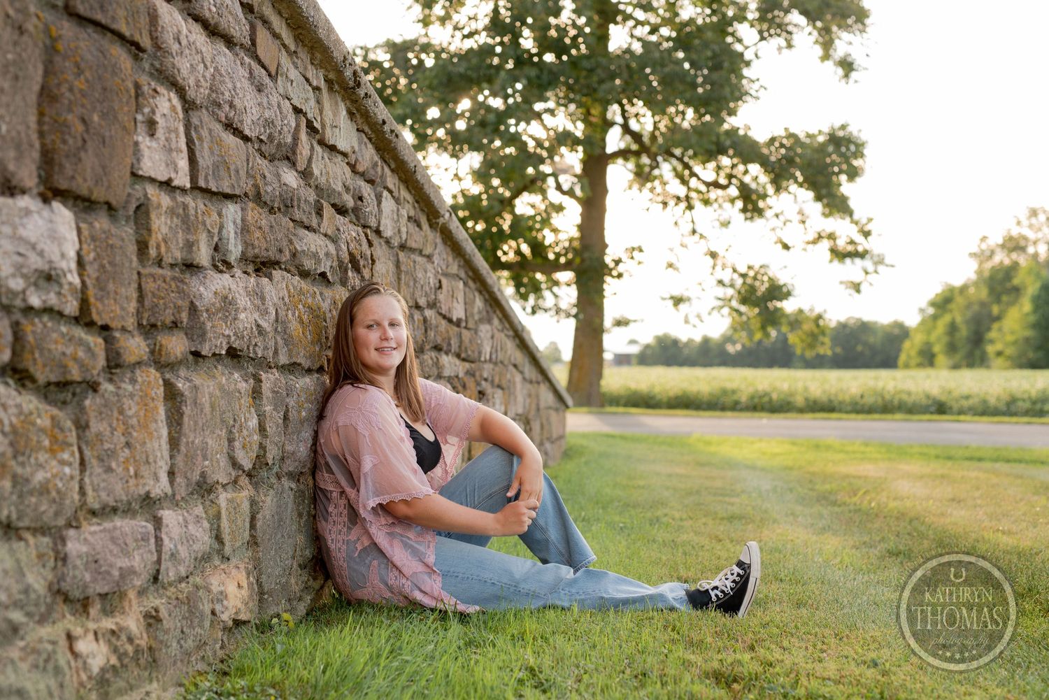Someone in casual attire sitting against a stone wall during golden hour.