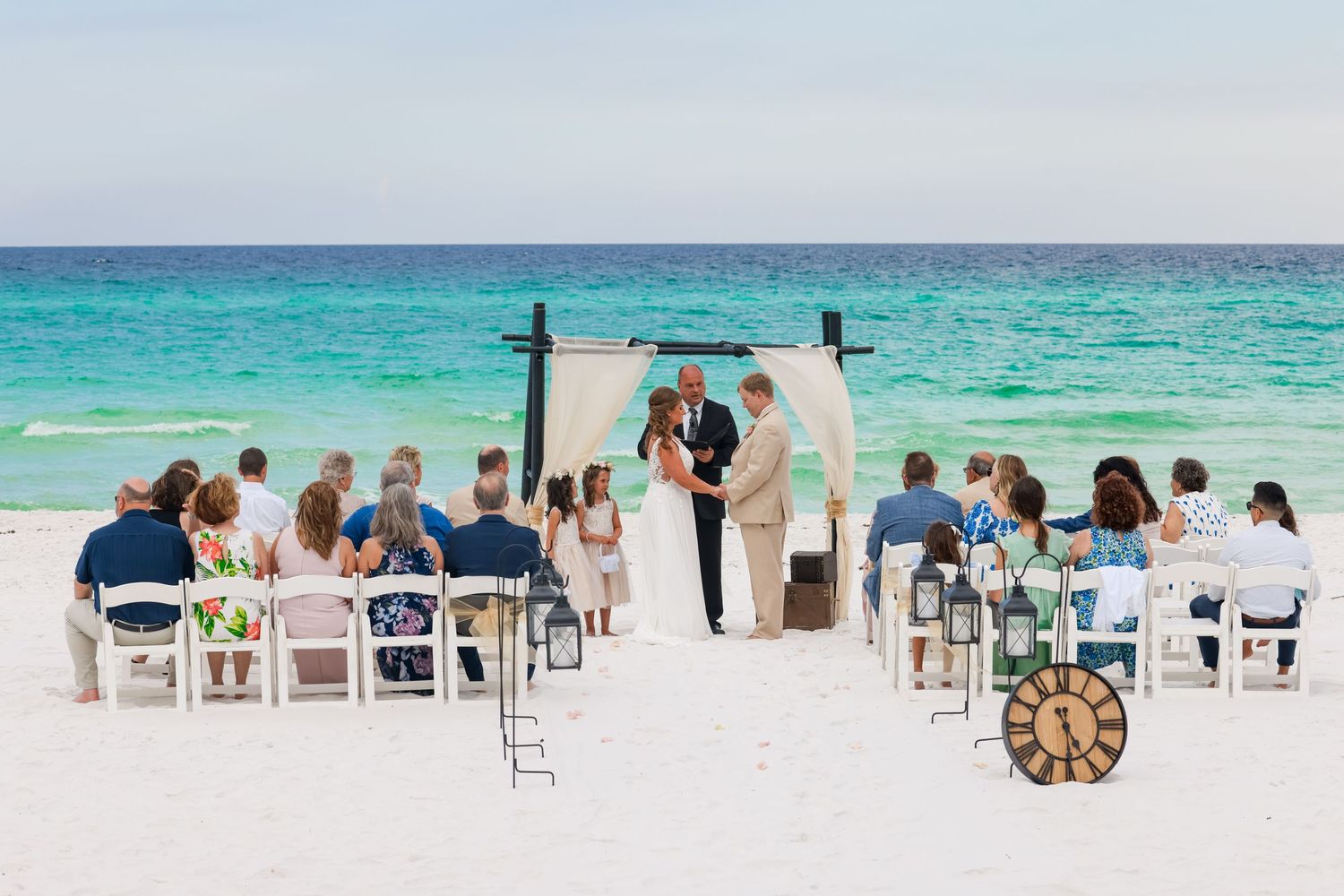 Beach wedding ceremony setup with white chairs and arch overlooking turquoise waters.