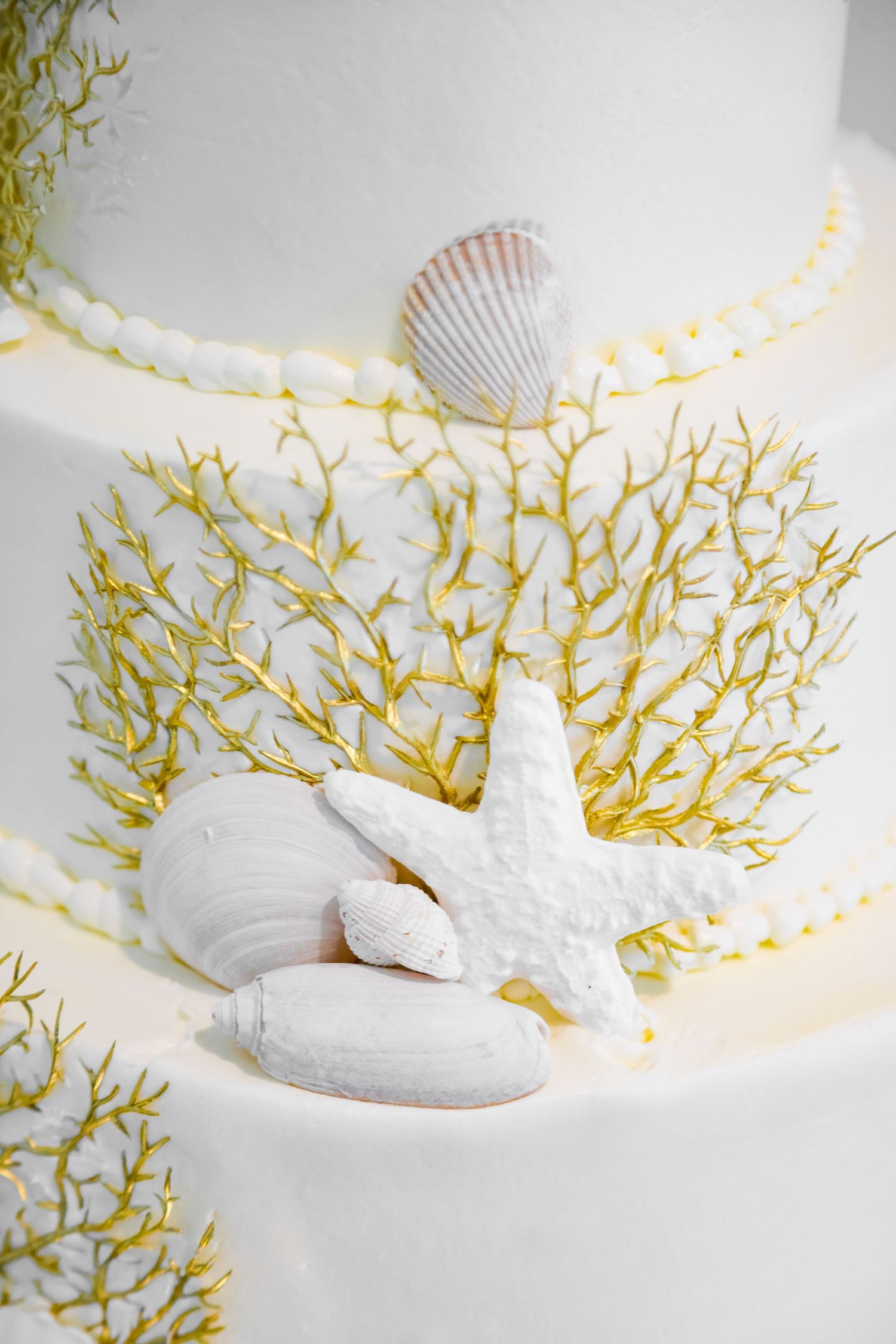 White wedding cake decorated with seashells, starfish, and yellow coral designs.