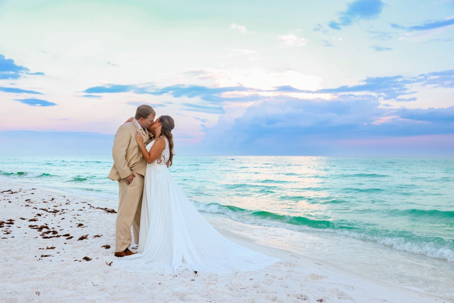 Romantic beach wedding portrait with couple kissing at sunset by the turquoise ocean.