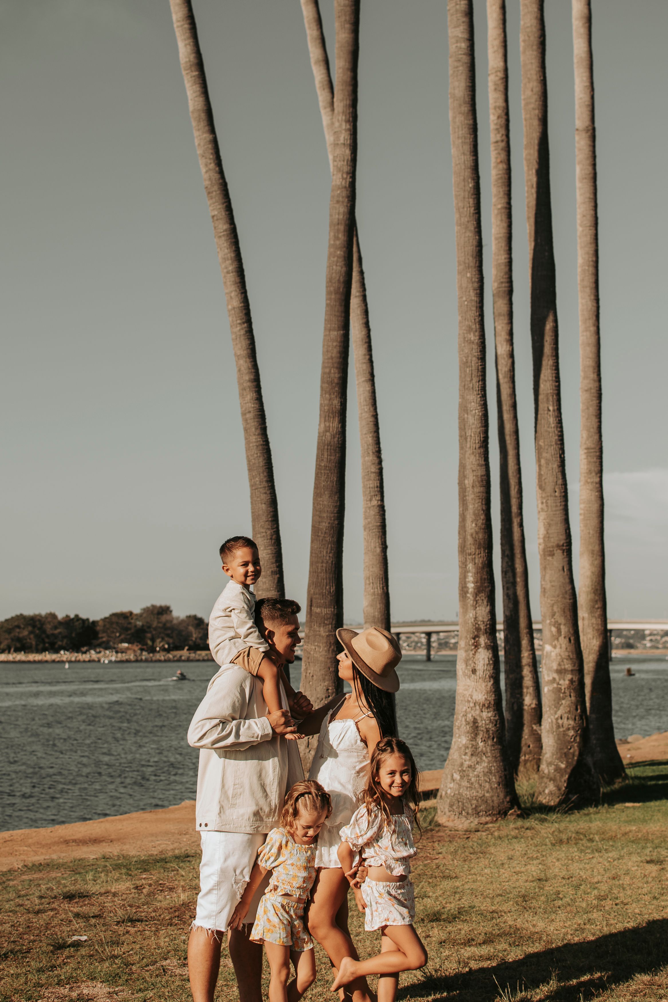 Family in white outfits posing near tall palm trees by the waterfront.