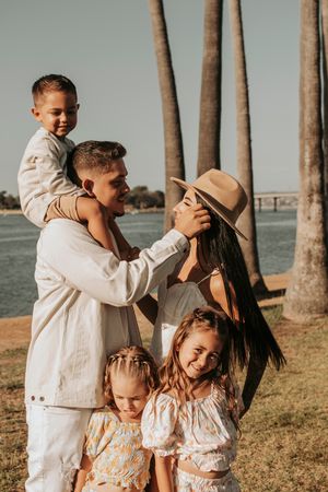 Playful family photo session in coordinated white outfits near palm trees.