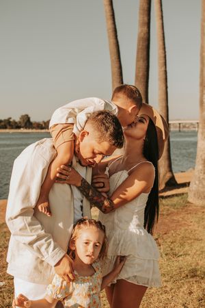 Loving family moment captured at sunset near palm trees by the water.