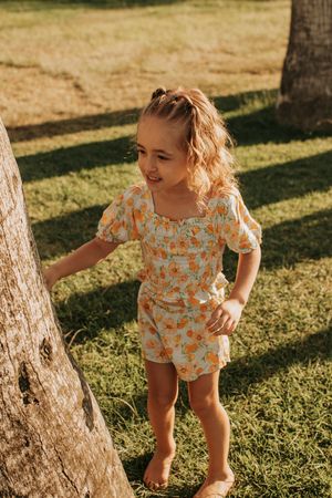 Toddler in a floral romper exploring between palm trees on a sunny afternoon.