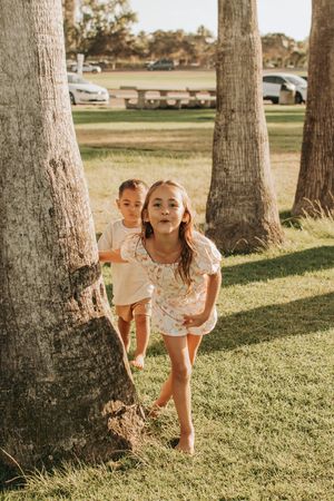 Playful hide and seek moment between palm trees on a grassy lawn at sunset.