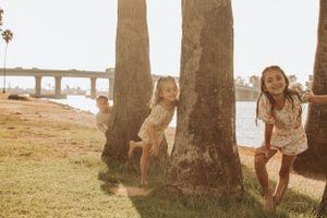 Family walking together through a palm tree grove at sunset near the water.