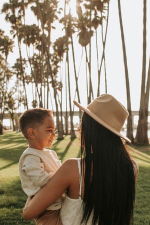 Sunlit portrait of parent and child embracing among palm trees at sunset.