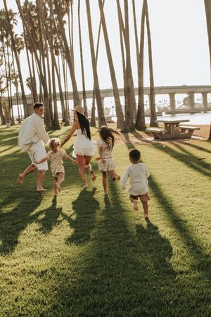 Family playing and running through palm trees during golden hour at the park.