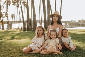 Family relaxing together on grassy lawn with palm trees at sunset in casual summer outfits.
