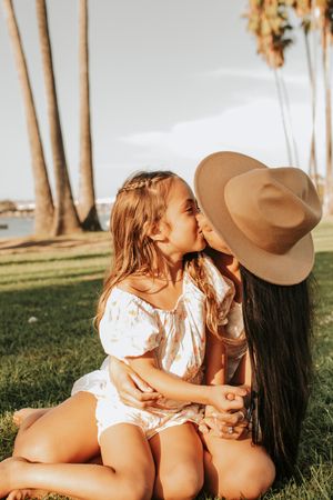 Two people in white outfits sharing an intimate moment on grass with palm trees in background.