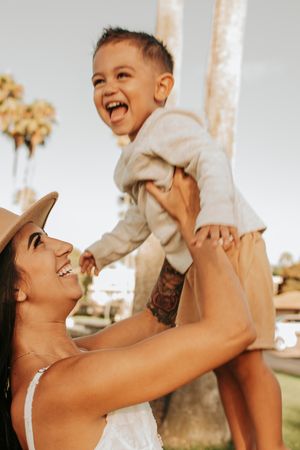 Joyful moment of parent lifting laughing child outdoors near palm trees.