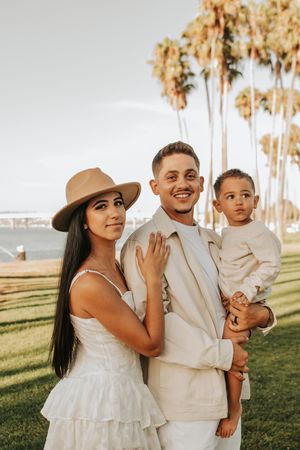 Family in coordinated white outfits posing together in outdoor setting with palm trees.