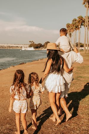 Family walking along beach path with palm trees at sunset.