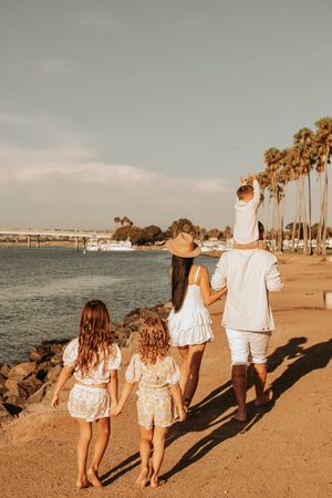 Silhouette of family walking together along waterfront with palm trees at golden hour.