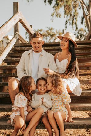 Happy family shares intimate moment on rustic wooden staircase during outdoor photoshoot.