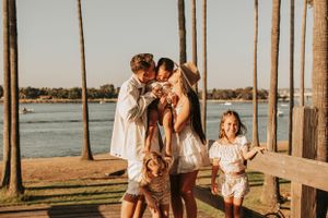 Joyful family moment captured at sunset by waterfront with palm trees in background.
