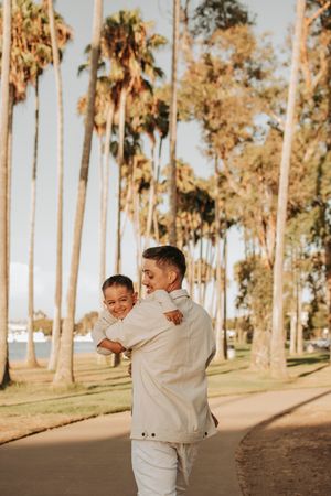 Parent and child share playful moment among towering palm trees at sunset.