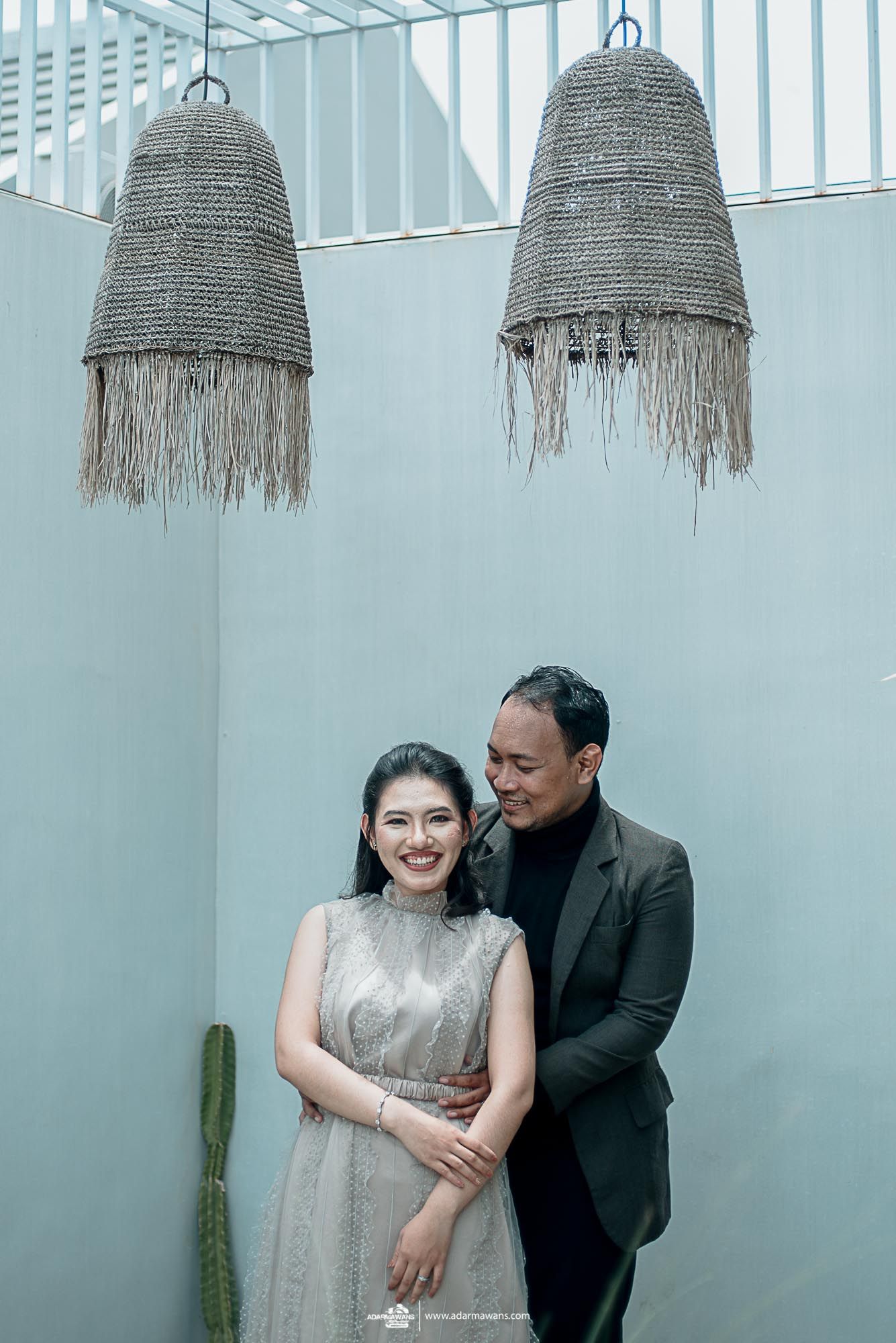 A couple poses beneath rustic hanging lamps in a modern interior space.