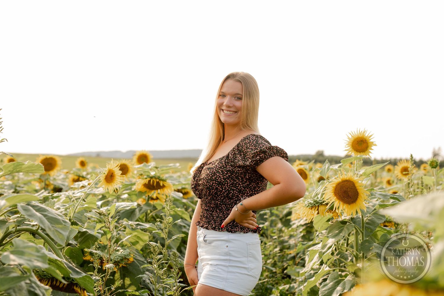 Woman posing in white shorts among blooming sunflowers during golden hour.