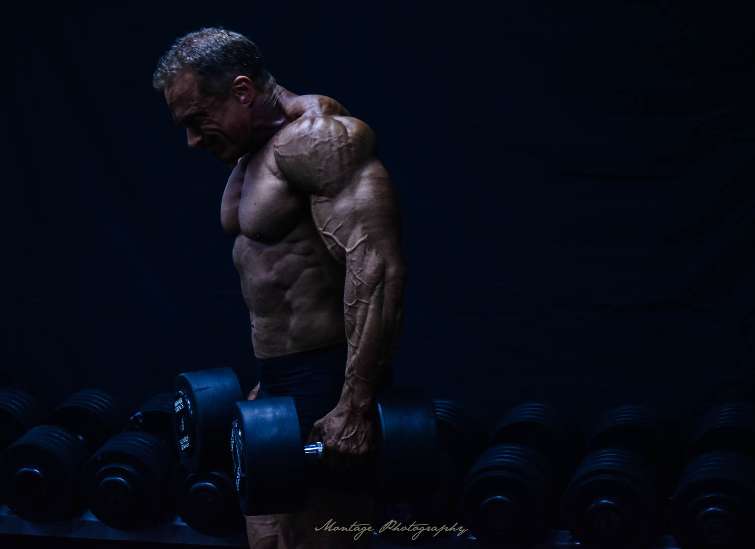 Bodybuilder with defined muscles lifting weights in moody dark gym setting.
