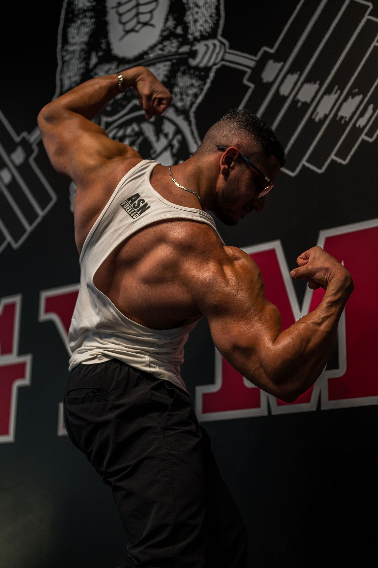 Muscular physique displayed in dramatic pose against gym wall with weight lifting artwork.