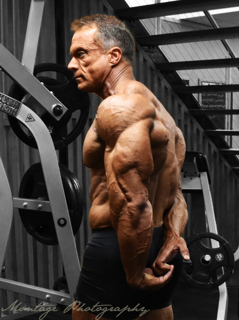 Side view of bodybuilder demonstrating muscular back development in gym setting.