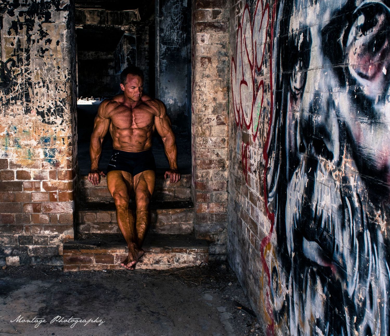 Strong physique posed in abandoned urban setting with artistic graffiti wall details.