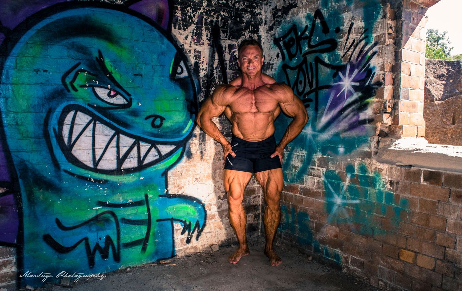 Muscular pose beside bright turquoise monster street art in urban setting.