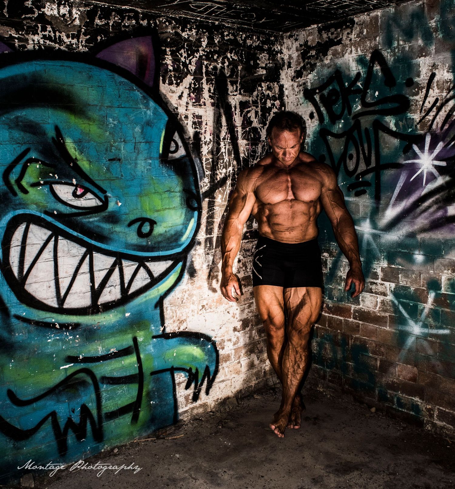 Muscular physique posed against urban graffiti wall featuring a large blue cartoon monster character.