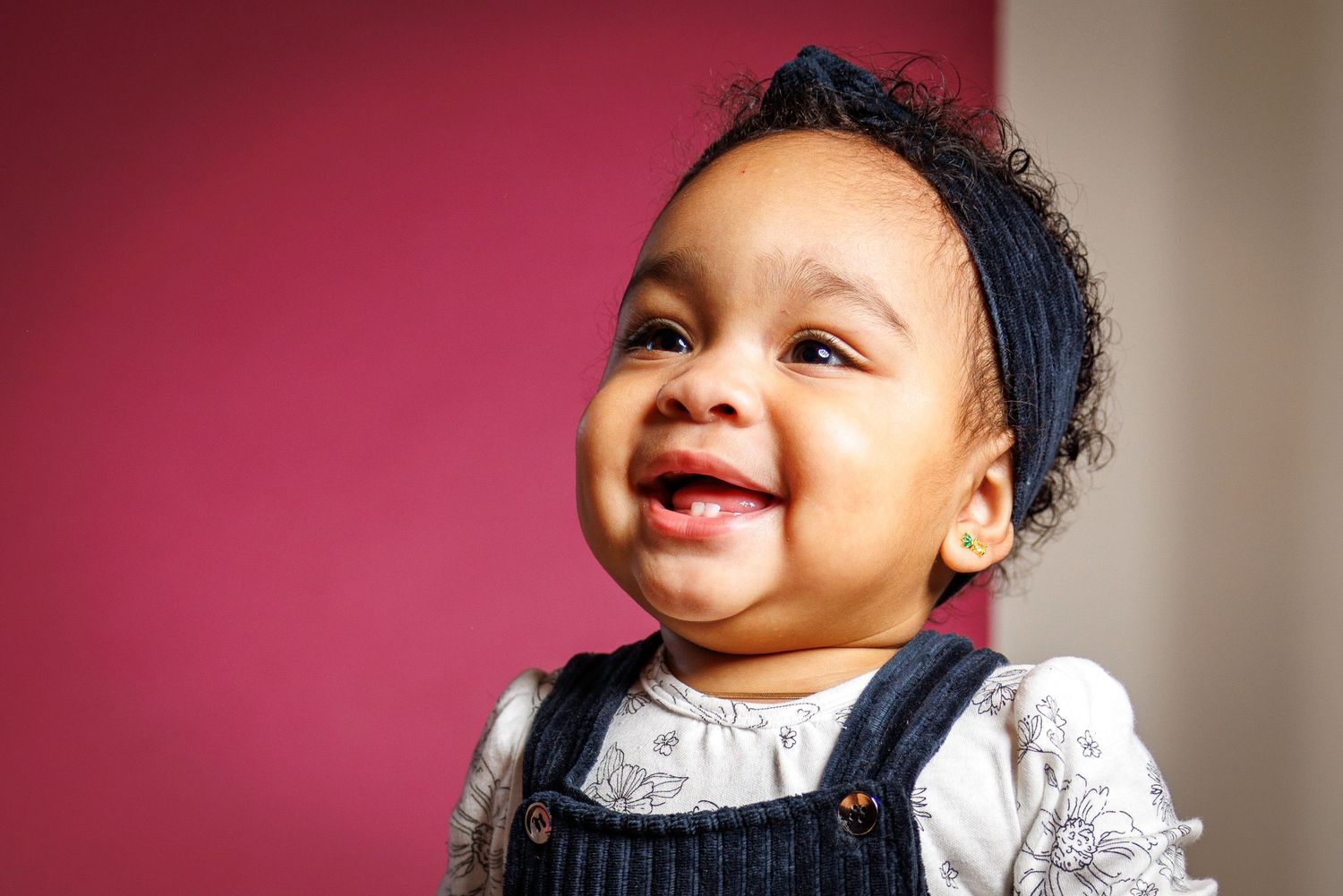 Baby wearing white outfit smiles and laughs in series of portrait photos against red background.