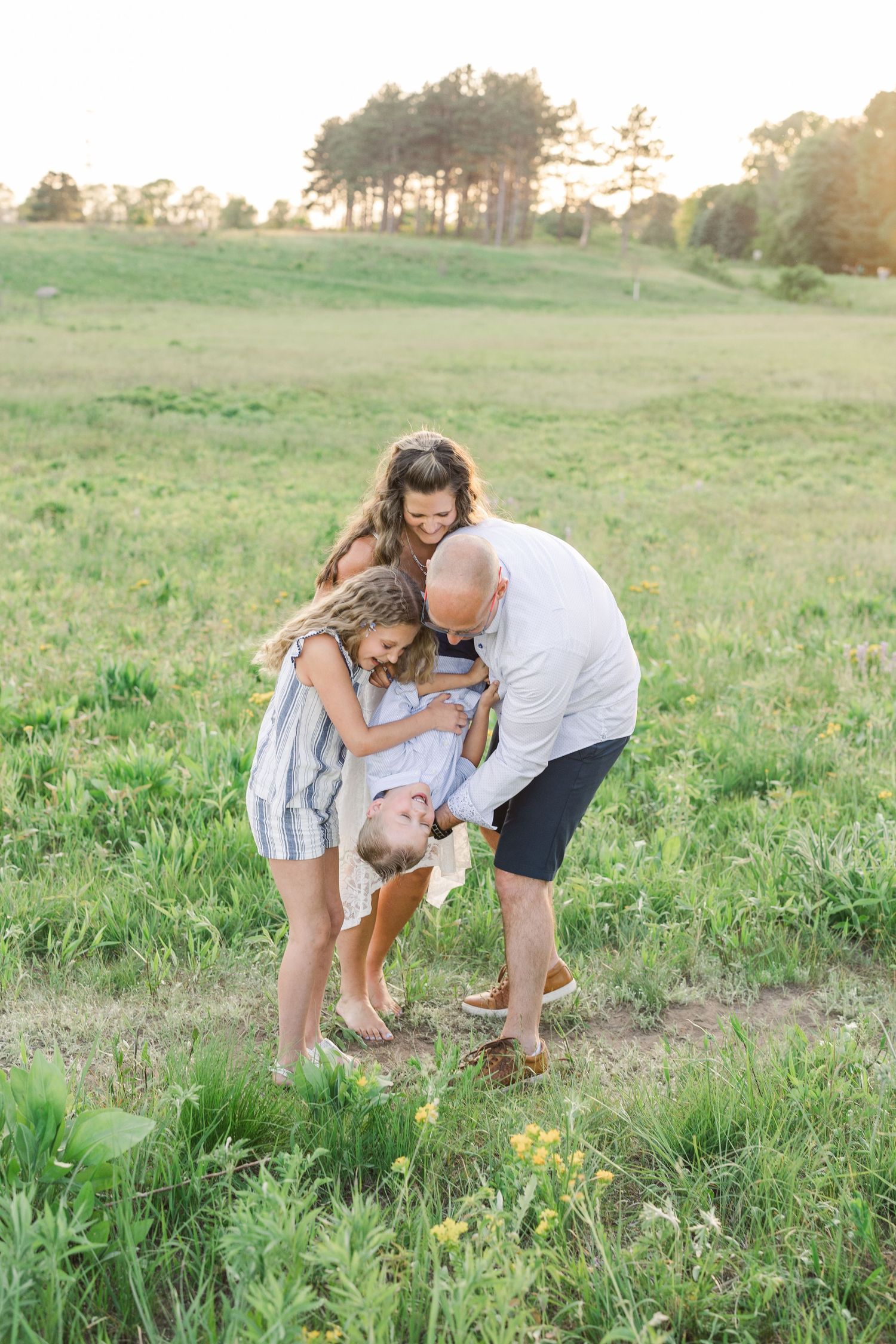 A tender family moment shared in a sunny green meadow during golden hour.