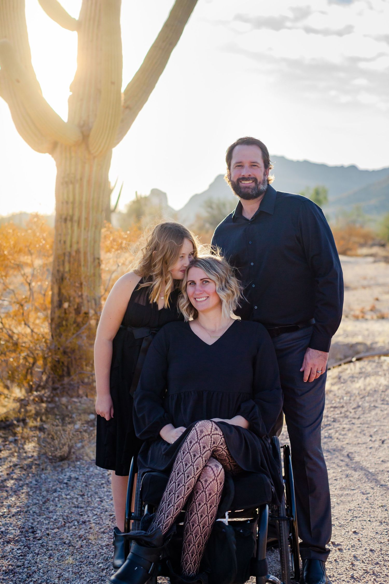 Family portrait in black attire against desert landscape with saguaro cactus at sunset.