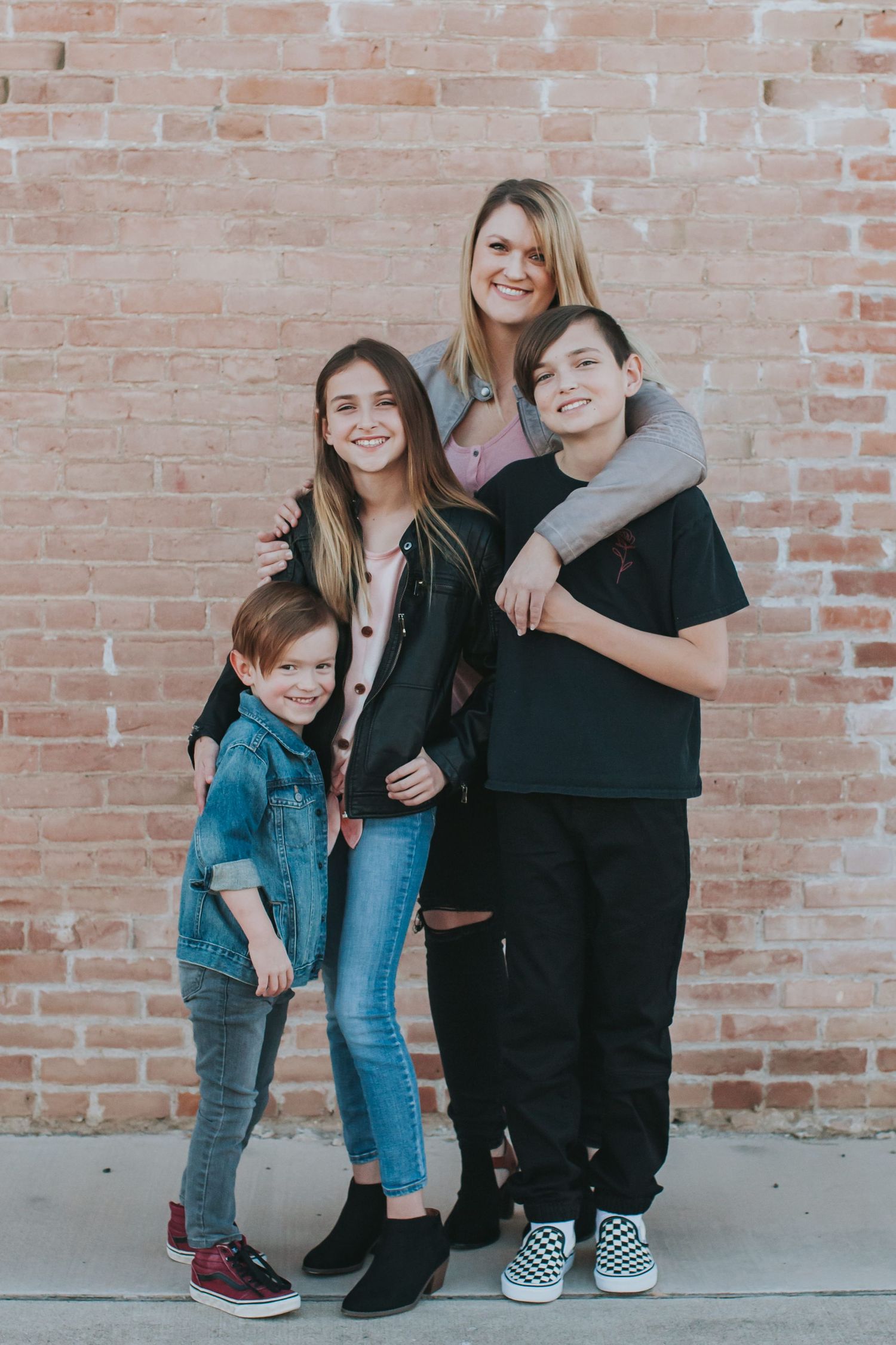 Family group poses casually against brick wall wearing coordinated casual outfits.