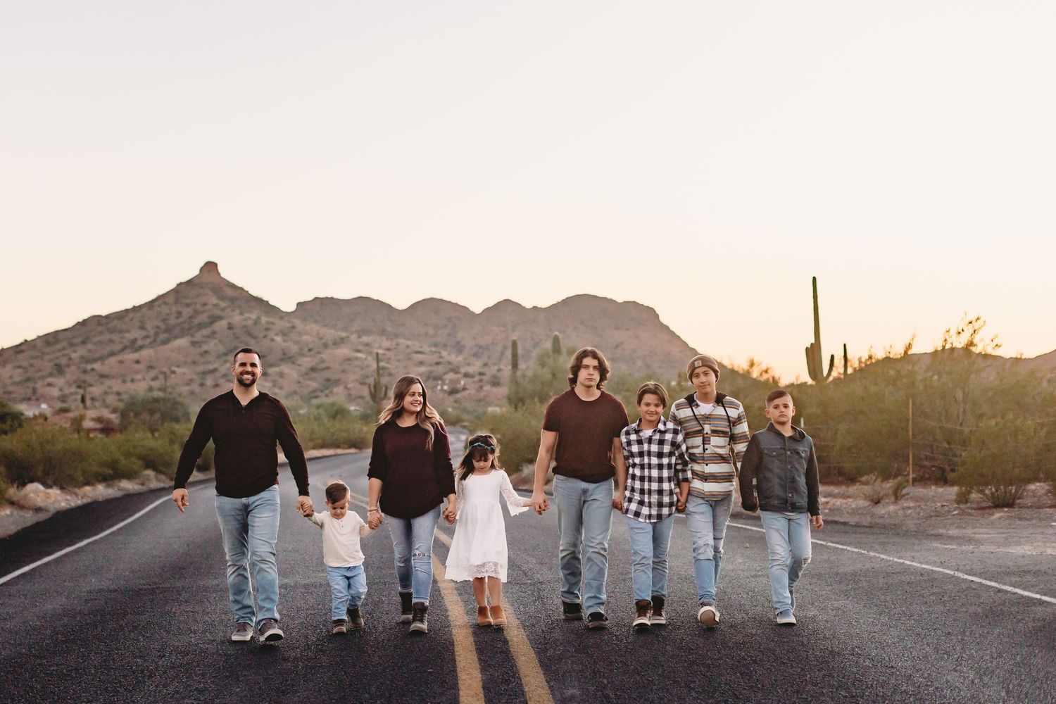 Wedding party poses in casual attire against scenic desert mountain backdrop at sunset.